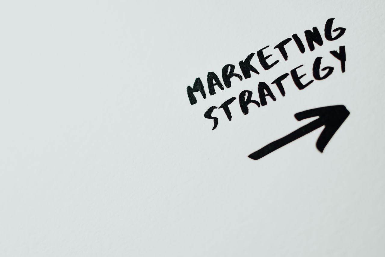 Close-up of handwritten Marketing Strategy text with an arrow on white background.